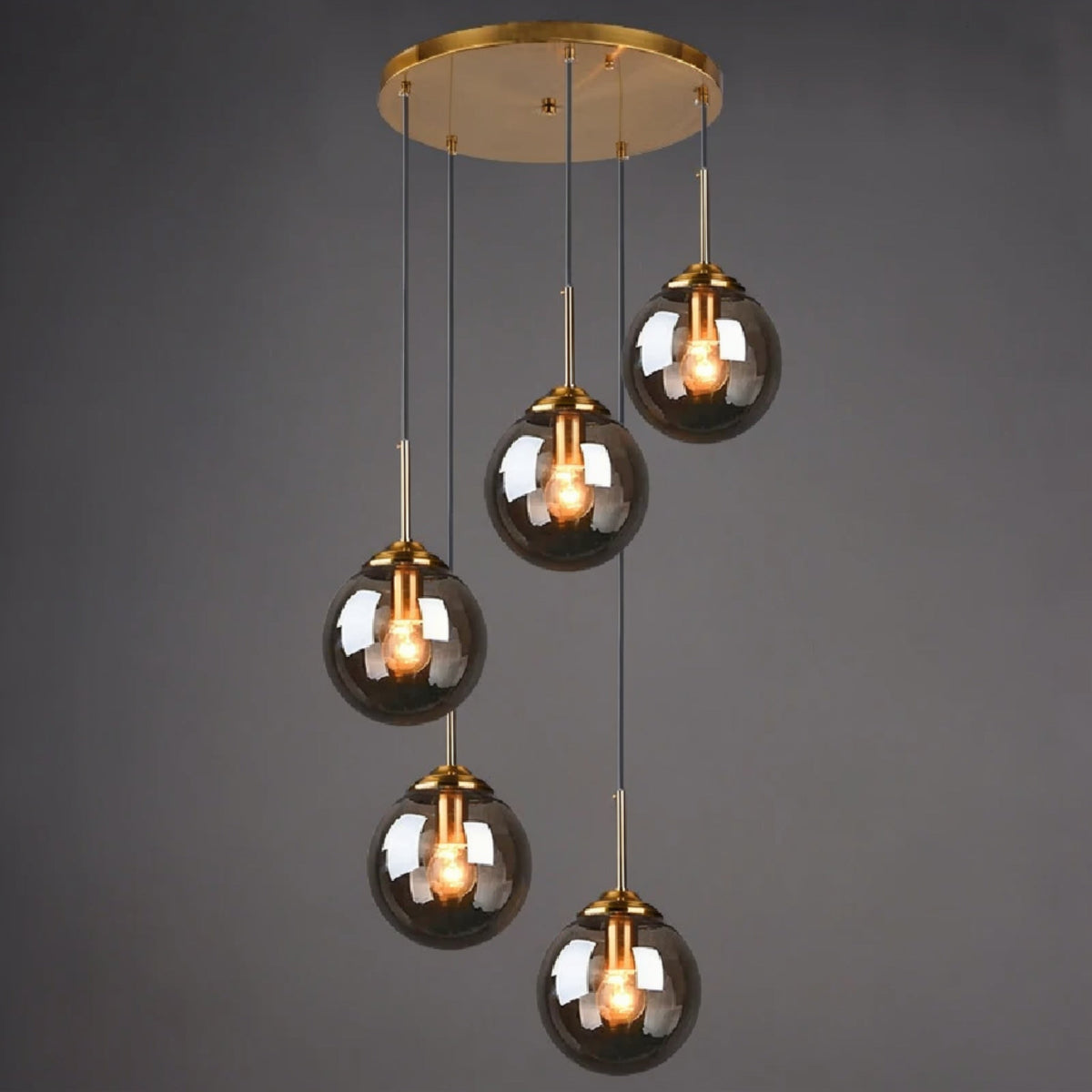Smoky grey glass globe pendant light, 5-light drop configuration in a staggered spiral cluster on gold cords from a round ceiling mount, lit against a dark grey background — LivDecor