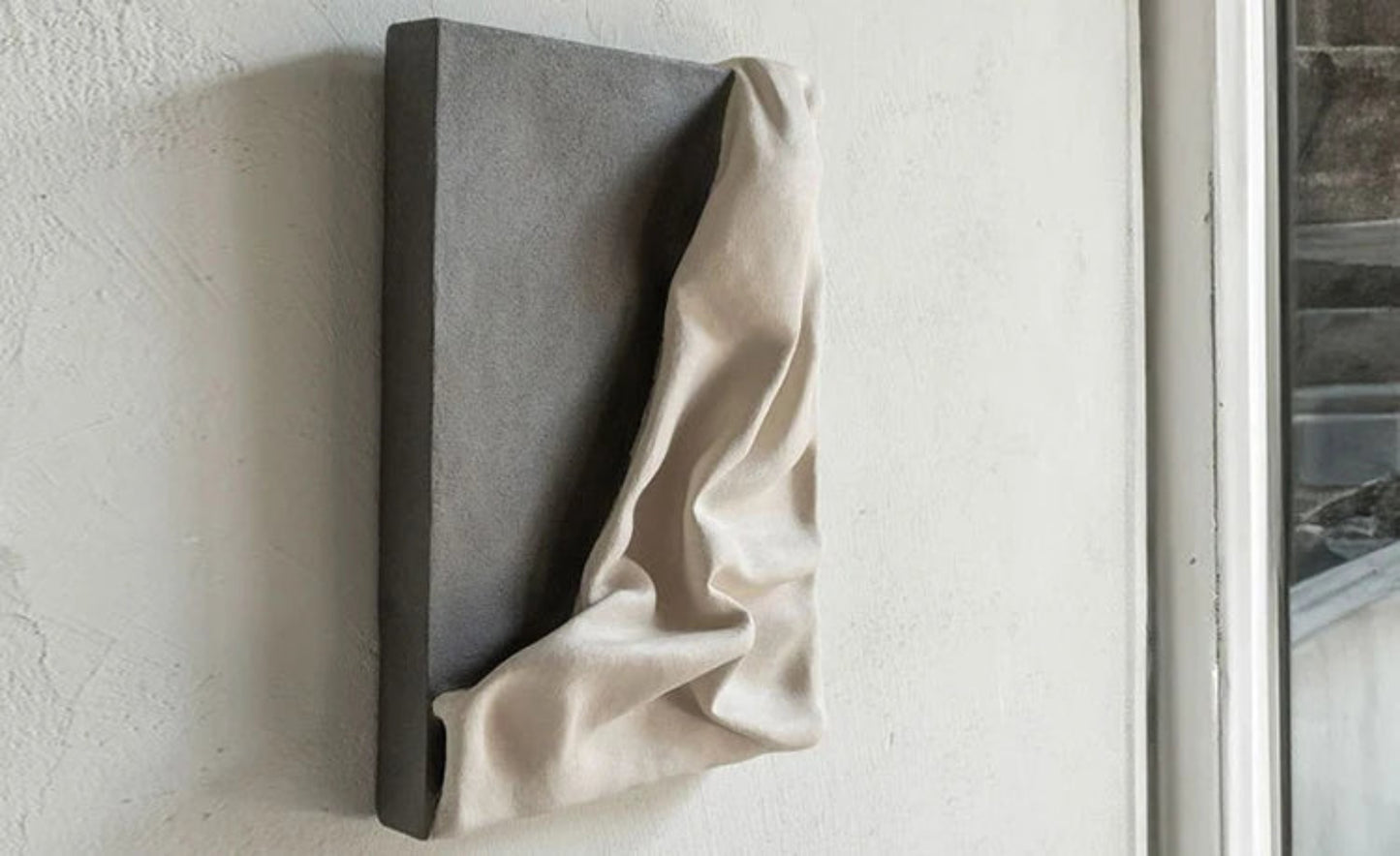 3D draped cream fabric resin wall sculpture on a charcoal grey panel mounted on a textured white wall, photographed at an angle to show depth and shadow detail — LivDecor