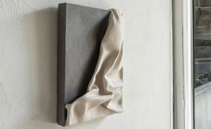 3D draped cream fabric resin wall sculpture on a charcoal grey panel mounted on a textured white wall, photographed at an angle to show depth and shadow detail — LivDecor