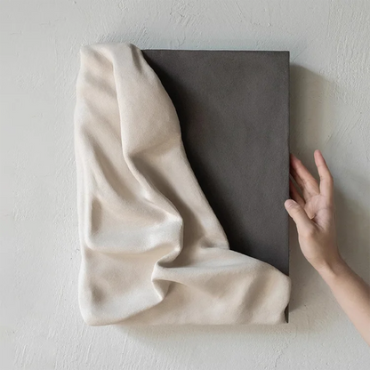 3D draped cream fabric resin wall sculpture on a charcoal grey panel with a hand placed beside it to show scale — LivDecor