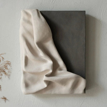 3D draped cream fabric resin wall sculpture on a charcoal grey panel mounted on a textured white wall with dried pampas grass in the lower left corner — LivDecor