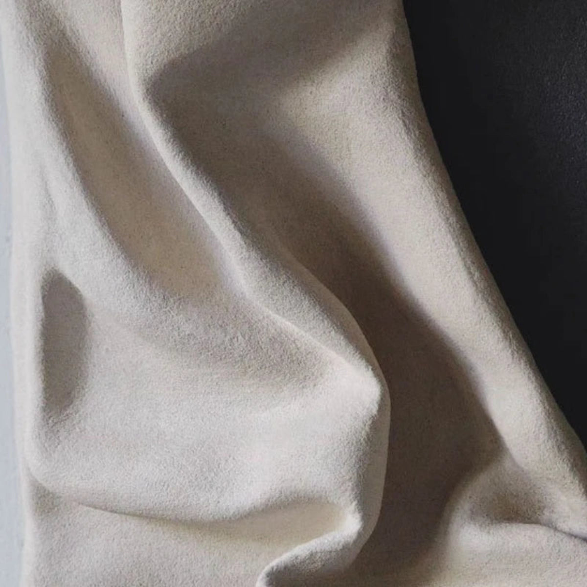 Macro close-up of 3D draped cream resin wall sculpture surface showing fine fabric texture and deep fold shadows against the charcoal panel edge — LivDecor