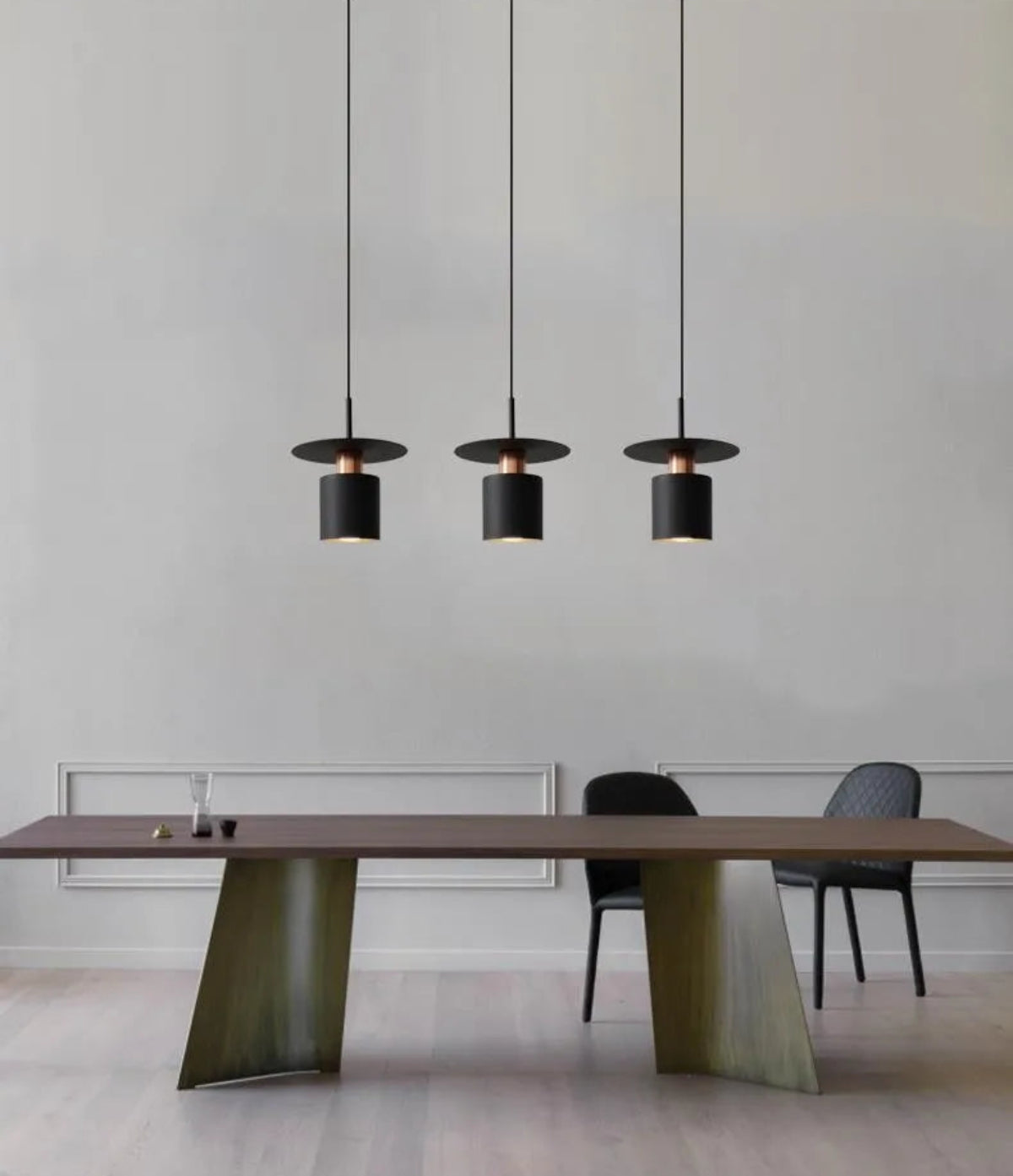 Three Aero Slim cylinder pendant lights in matte black with copper accent hung in a linear row over a walnut and olive green trestle dining table with black shell chairs against a white panelled wall — LivDecor
