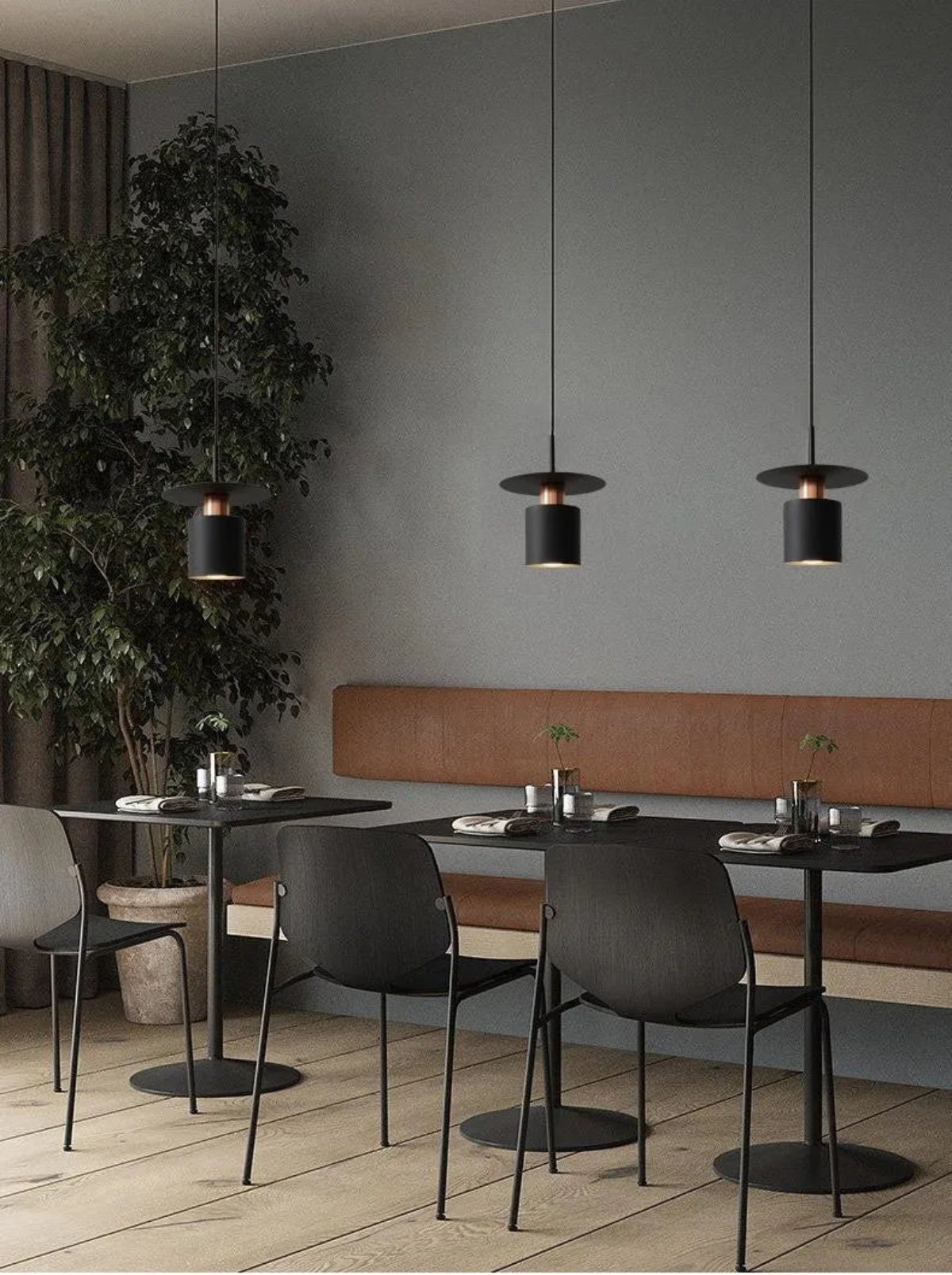 Three Aero Slim cylinder pendant lights in matte black with copper accent hung at staggered heights over bistro tables with cork banquette seating against slate blue walls in a moody restaurant setting — LivDecor
