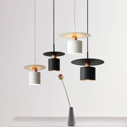 Four Aero Slim cylinder pendant lights in matte black and white with copper accent hung at staggered heights alongside a single allium stem in a concrete vase on a white background — LivDecor
