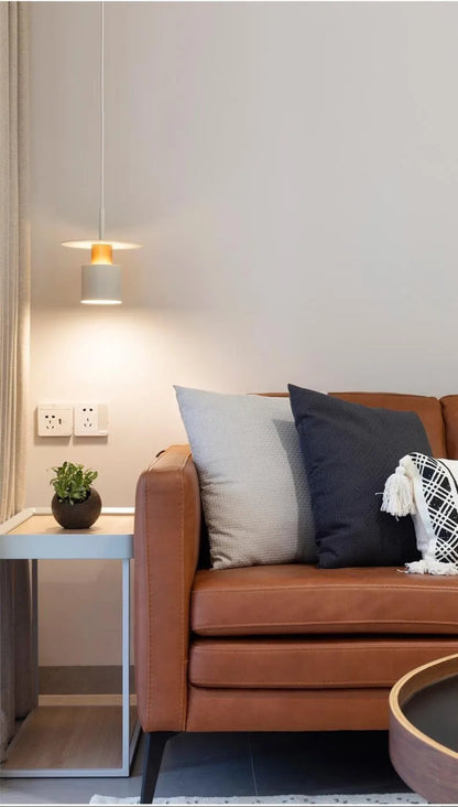 Aero Slim cylinder pendant light in matte white with copper accent lit beside a tan leather sofa with side table and potted plant in a minimalist living room — LivDecor
