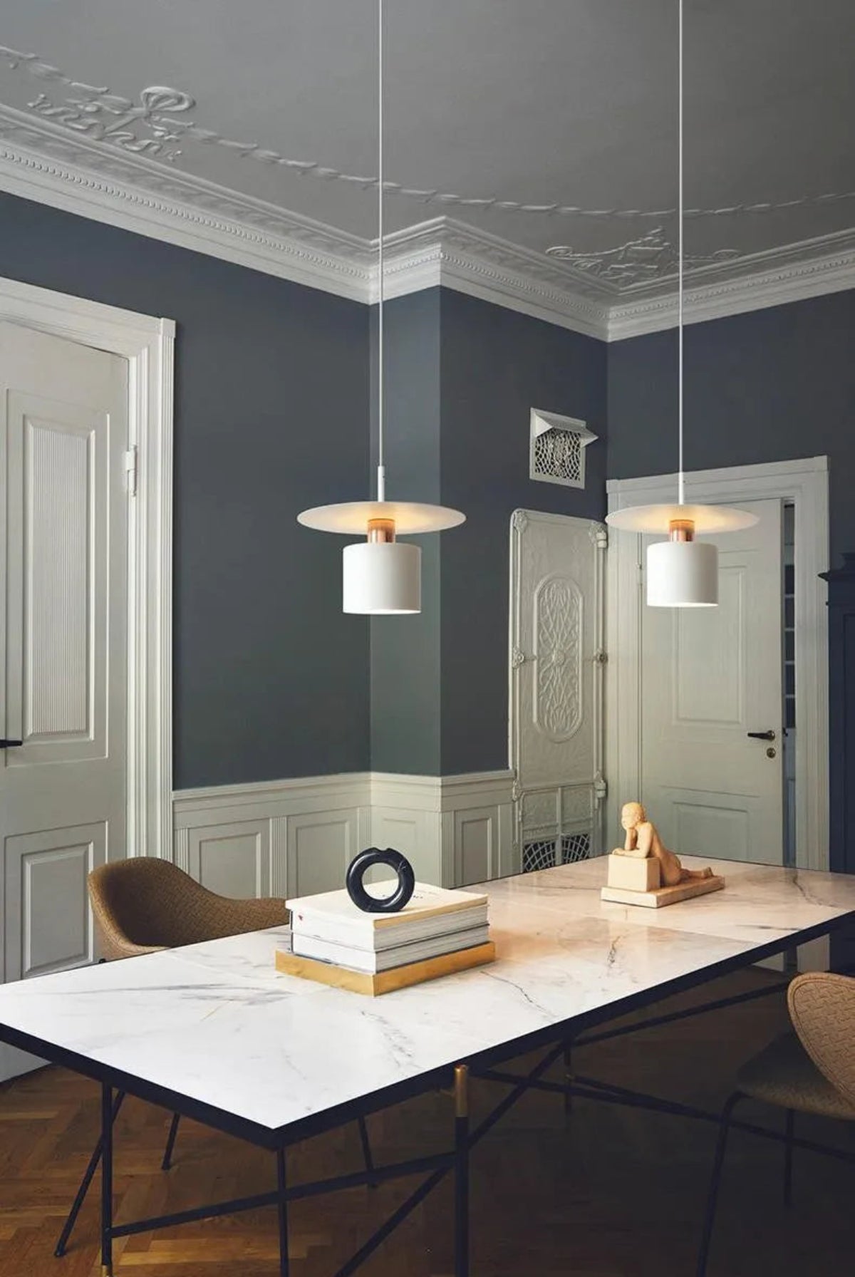 Two Aero Slim cylinder pendant lights in matte white with copper accent hung in a pair over a marble dining island in a grand Haussmann-style room with dark slate walls and ornate crown molding — LivDecor

