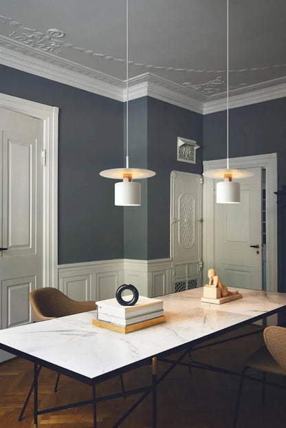 Two Aero Slim cylinder pendant lights in matte white with copper accent hung in a pair over a marble dining island in a grand Haussmann-style room with dark slate walls and ornate crown molding — LivDecor
