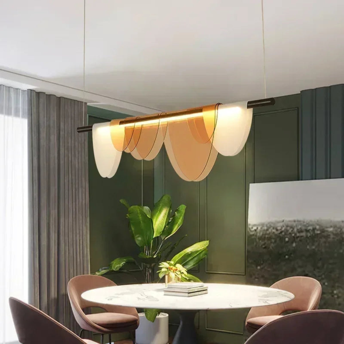 Amber acrylic petal pendant light with five petals illuminated above a round marble dining table with blush velvet chairs against deep forest green paneled walls with a tropical plant — LivDecor