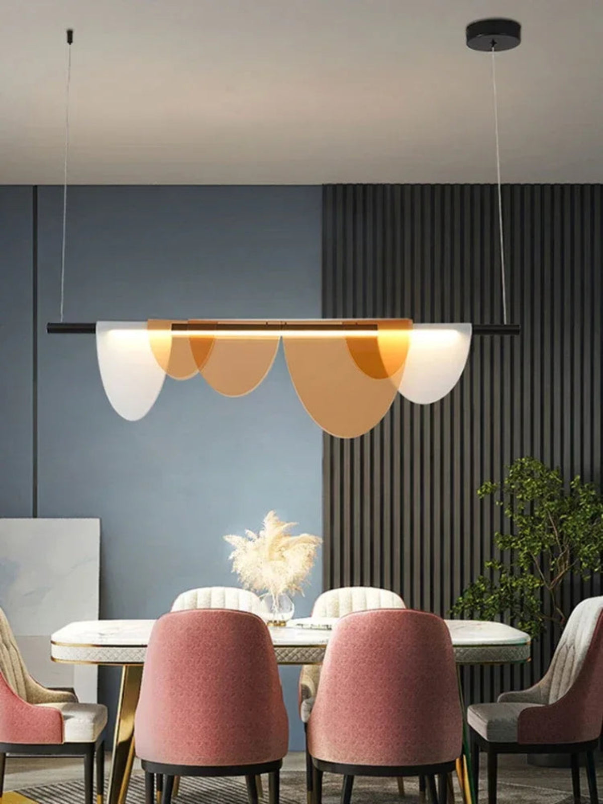Amber acrylic petal pendant light illuminated above a white marble dining table with blush pink velvet chairs against a slate blue wall with slatted wood panel — LivDecor