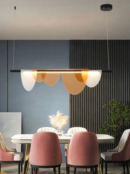 Amber acrylic petal pendant light illuminated above a white marble dining table with blush pink velvet chairs against a slate blue wall with slatted wood panel — LivDecor