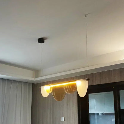 Amber acrylic petal pendant light installed in a real room showing the black ceiling canopy, steel cable drop, and warm LED glow against a neutral ceiling — LivDecor