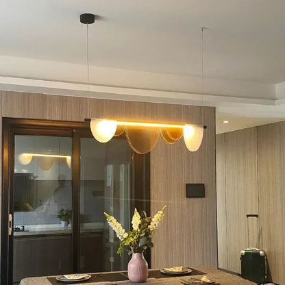 Amber acrylic petal pendant light installed above a dining table with place settings and a pink vase with white flowers in a real home setting — LivDecor