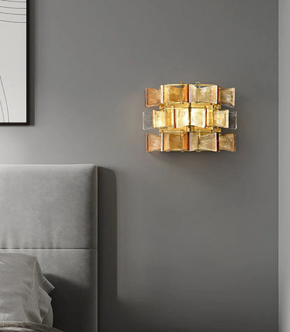 Amber and clear ribbed glass iron wall sconce with gold frame mounted on a grey wall above a modern upholstered bed in a contemporary bedroom — LivDecor