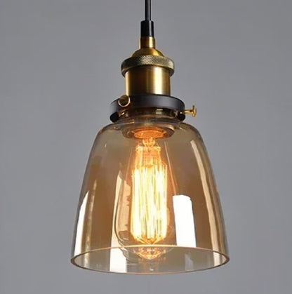 Amber glass bell-shaped pendant light with brass Edison fitting and lit filament bulb glowing warmly against a grey background — LivDecor
