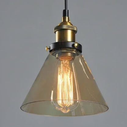 Amber glass cone-shaped pendant light with brass Edison fitting and lit filament bulb glowing warmly against a grey background — LivDecor
