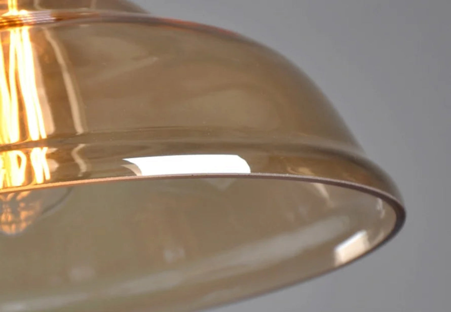 Close-up detail of amber glass dome pendant light showing smooth curved glass edge and warm Edison filament glow — LivDecor