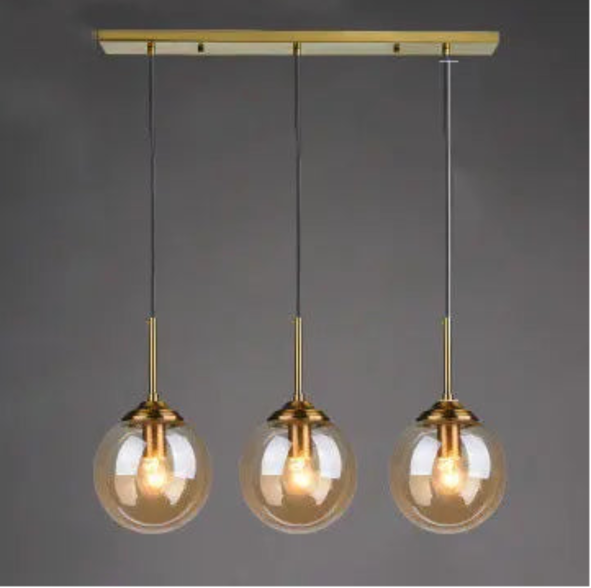 Three amber glass globe pendant lights evenly spaced on gold cords and rectangular bar ceiling mount in a linear row against a dark grey background — LivDecor
