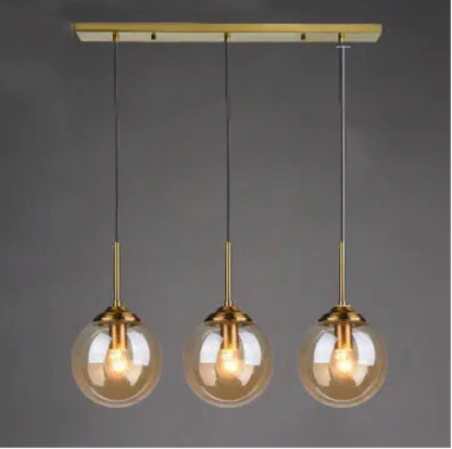 Three amber glass globe pendant lights evenly spaced on gold cords and rectangular bar ceiling mount in a linear row against a dark grey background — LivDecor
