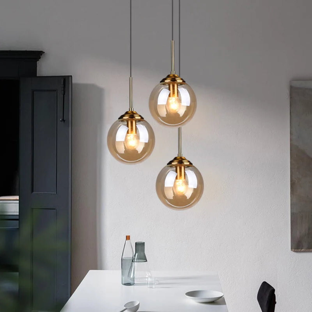 Three amber glass globe pendant lights hanging at staggered heights above a white kitchen counter with dark grey cabinetry in a modern contemporary kitchen — LivDecor
