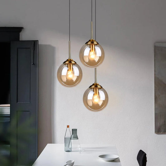 Three amber glass globe pendant lights hanging at staggered heights above a white kitchen counter with dark grey cabinetry in a modern contemporary kitchen — LivDecor
