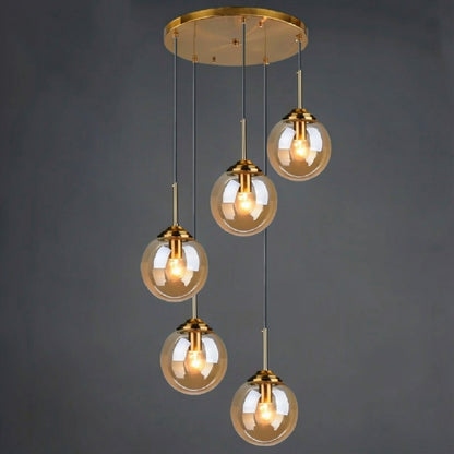 Amber glass globe pendant light, 5-light drop configuration in a staggered spiral cluster on gold cords from a round ceiling mount, lit against a dark grey background — LivDecor
