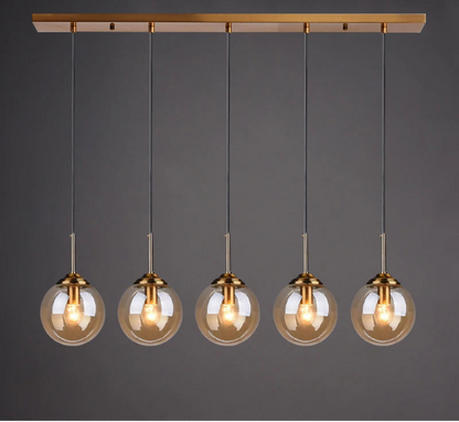 Five amber glass globe pendant lights evenly spaced on gold cords and rectangular bar ceiling mount in a linear row against a dark grey background — LivDecor
