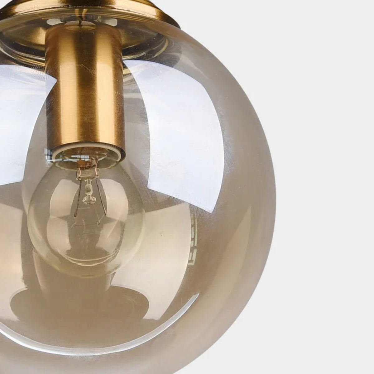 Close-up detail of an amber glass globe pendant light showing brushed gold fitting and Edison filament bulb against a white background — LivDecor

