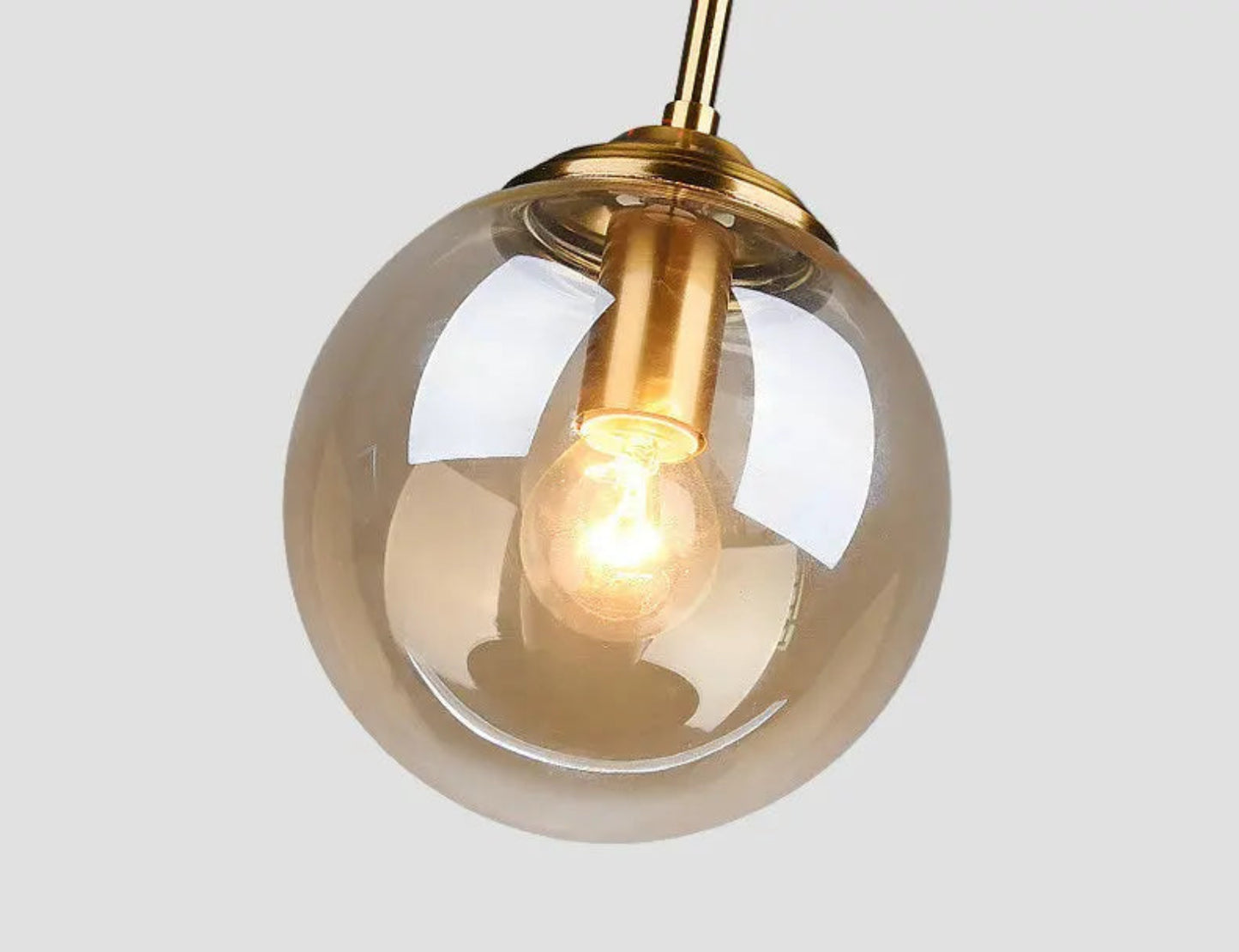 Close-up of an amber glass globe pendant light with warm glowing filament bulb and brushed gold hardware fitting against a light grey background — LivDecor
