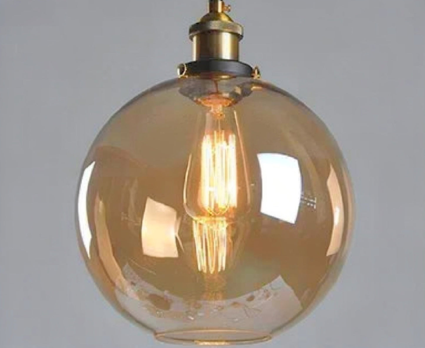 Amber glass globe pendant light with brass Edison fitting and lit filament bulb glowing warmly against a grey background — LivDecor
