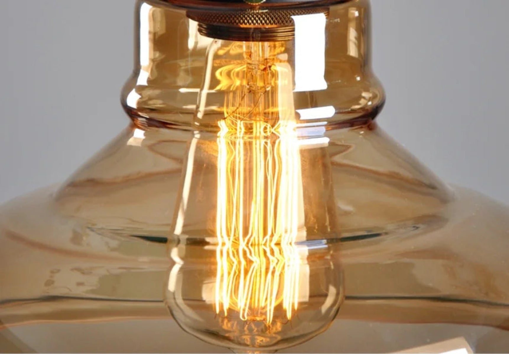 Close-up macro detail of an amber glass pendant light showing a glowing squirrel cage Edison filament through the warm honey-toned glass — LivDecor