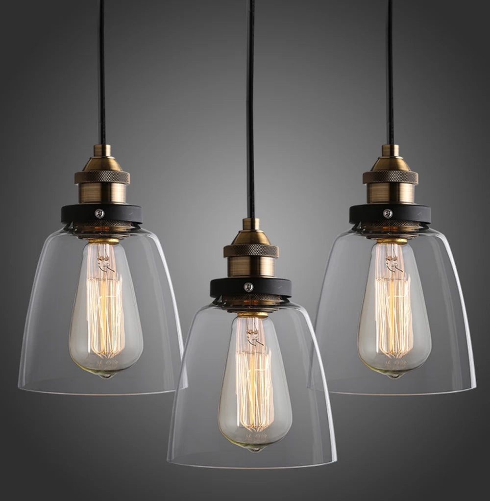Three clear glass cone pendant lights with antique brass and black sockets and glowing Edison filament bulbs on black cords against a dark gray background — LivDecor
