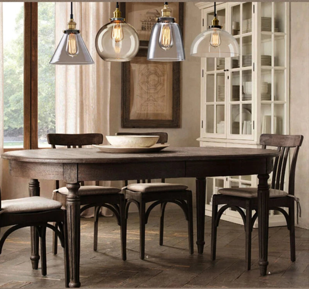 Three clear glass pendant lights in cone, globe, and dome styles with antique brass sockets and Edison filament bulbs above a dark rustic farmhouse dining table with a white hutch and linen drapes — LivDecor

