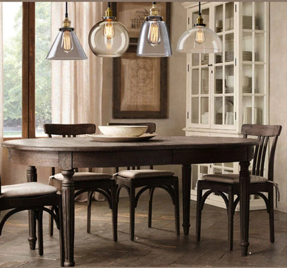 Three clear glass pendant lights in cone, globe, and dome styles with antique brass sockets and Edison filament bulbs above a dark rustic farmhouse dining table with a white hutch and linen drapes — LivDecor
