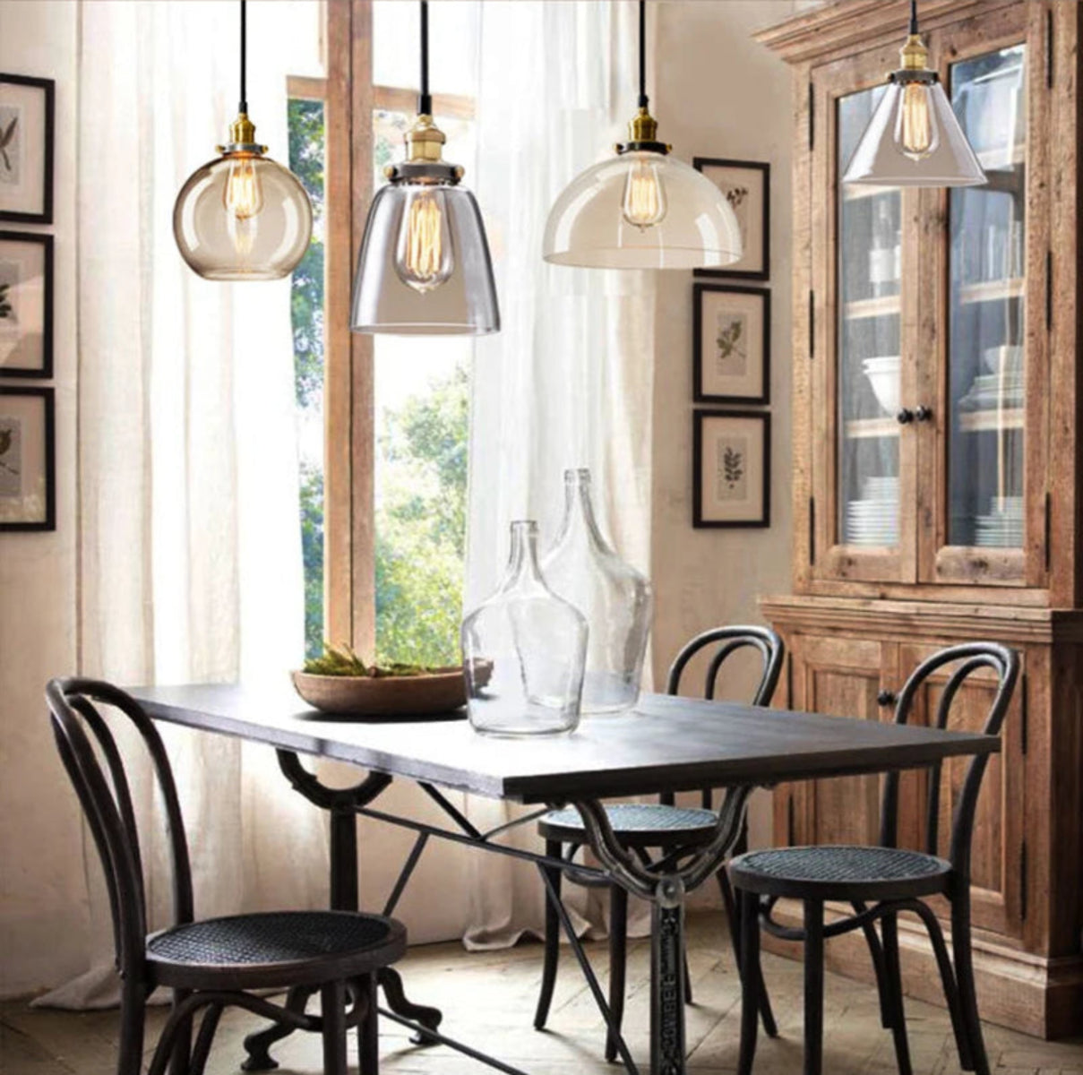 Three clear glass pendant lights in globe, bell, and dome styles with antique brass sockets and Edison filament bulbs above a rustic French country dining table with bistro chairs and a wood hutch — LivDecor