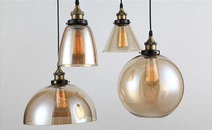Close-up detail of four amber iridescent glass pendant lights — bell, cone, dome, and globe — with antique brass sockets and glowing Edison filament bulbs on black cords — LivDecor
