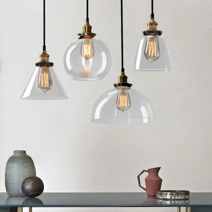 Four clear glass pendant lights — cone, globe, bell, and dome styles — with antique brass sockets and Edison filament bulbs above a styled shelf with ceramic vases and a terracotta jug against a warm white wall — LivDecor

