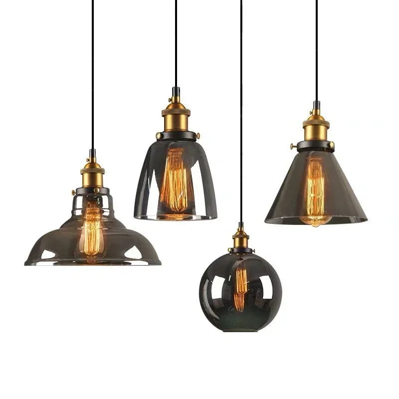 Four smoky gray glass pendant light styles with antique brass sockets and Edison filament bulbs on black cords against a white background — barn, bell, cone, and globe — LivDecor
