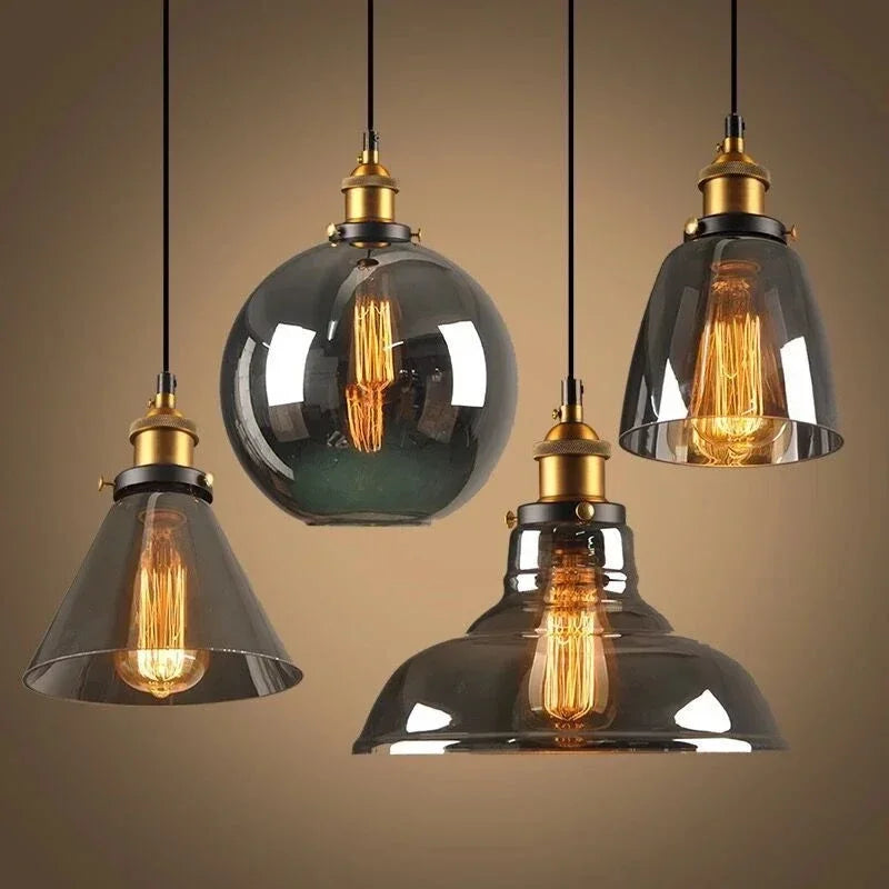 Four smoky gray glass pendant light styles with antique brass sockets and glowing Edison filament bulbs on black cords — cone, globe, wide barn, and bell — LivDecor