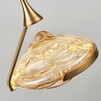 Close-up detail of an amber wave glass geometric pendant light glowing from within with swirling glass texture and brushed gold stem and ring hardware — LivDecor