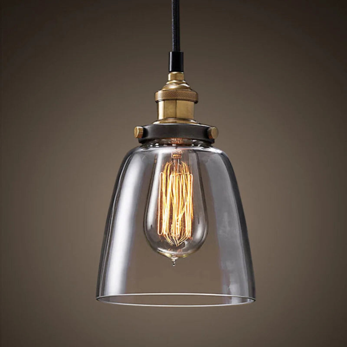 Single clear glass bell pendant light with antique brass socket and glowing Edison filament bulb on black cord against a dark moody background — LivDecor
