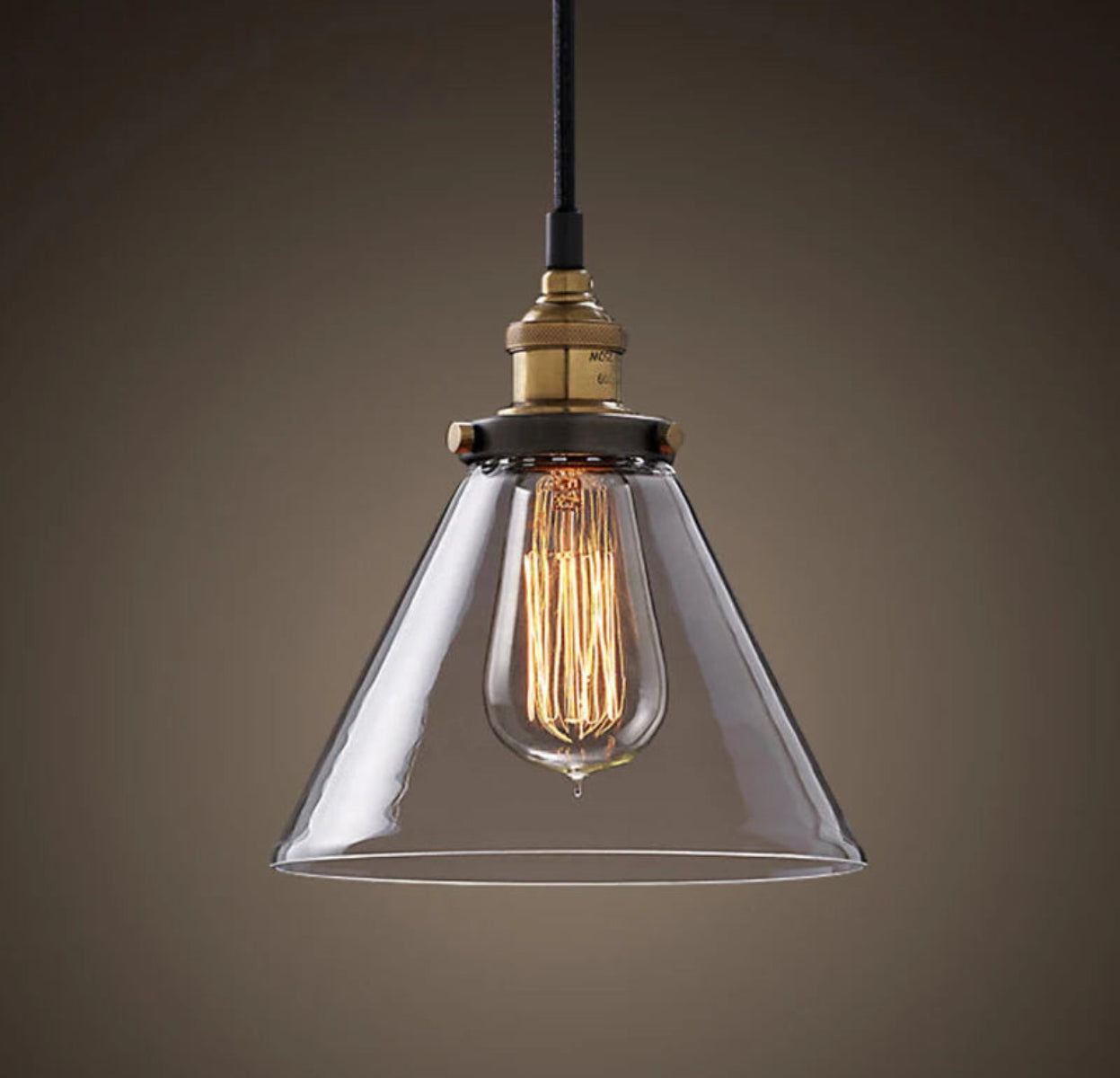 Single clear glass cone pendant light with antique brass socket and glowing Edison filament bulb on black cord against a dark moody background — LivDecor
