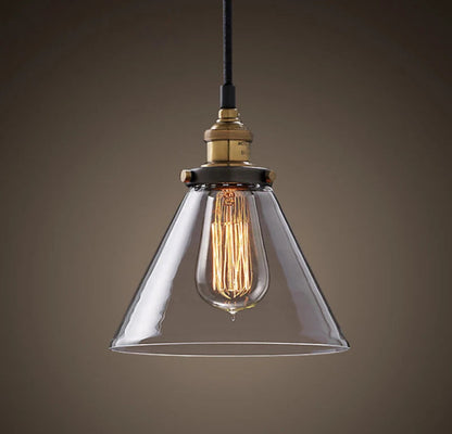 Single clear glass cone pendant light with antique brass socket and glowing Edison filament bulb on black cord against a dark moody background — LivDecor
