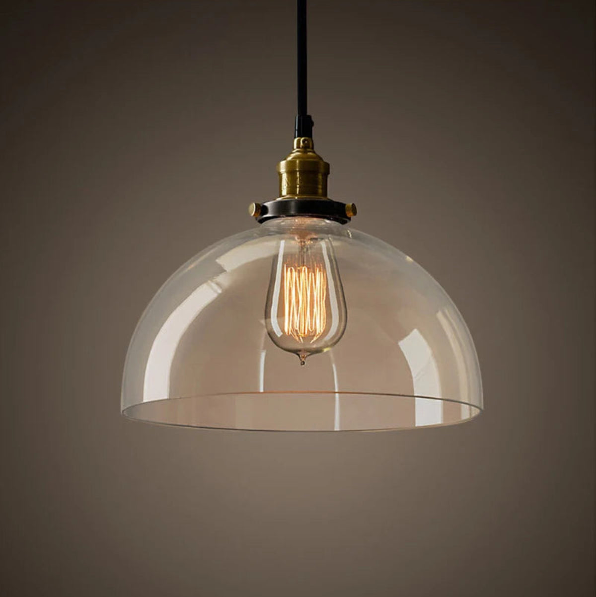 Single clear glass dome pendant light with antique brass socket and glowing Edison filament bulb on black cord against a dark moody background — LivDecor
