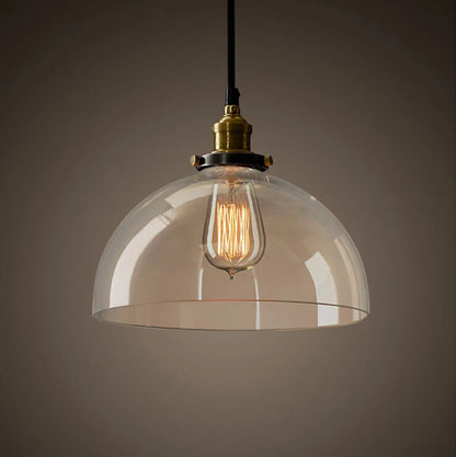 Single clear glass dome pendant light with antique brass socket and glowing Edison filament bulb on black cord against a dark moody background — LivDecor
