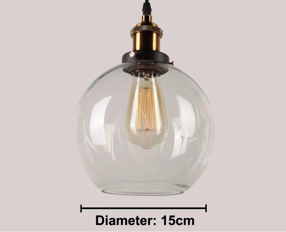 Close-up of a single clear glass globe pendant light with antique brass and black socket and glowing Edison filament bulb on black cord, 15cm diameter — LivDecor
