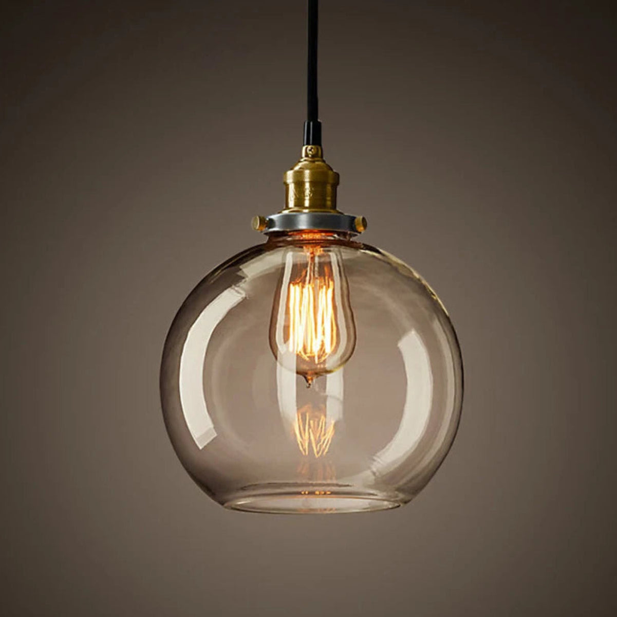 Single clear glass globe pendant light with antique brass socket and glowing Edison filament bulb on black cord against a dark moody background — LivDecor
