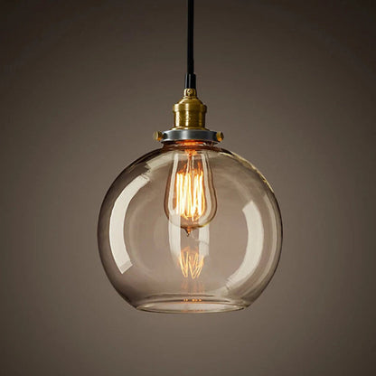 Single clear glass globe pendant light with antique brass socket and glowing Edison filament bulb on black cord against a dark moody background — LivDecor
