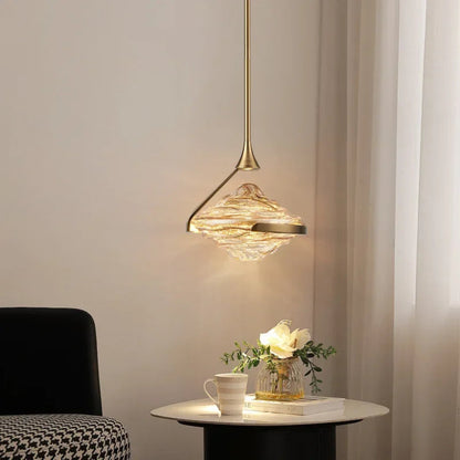 Single amber wave glass geometric pendant light on a gold stem glowing warmly above a marble side table with rose vase and teacup in a cozy living room corner — LivDecor
