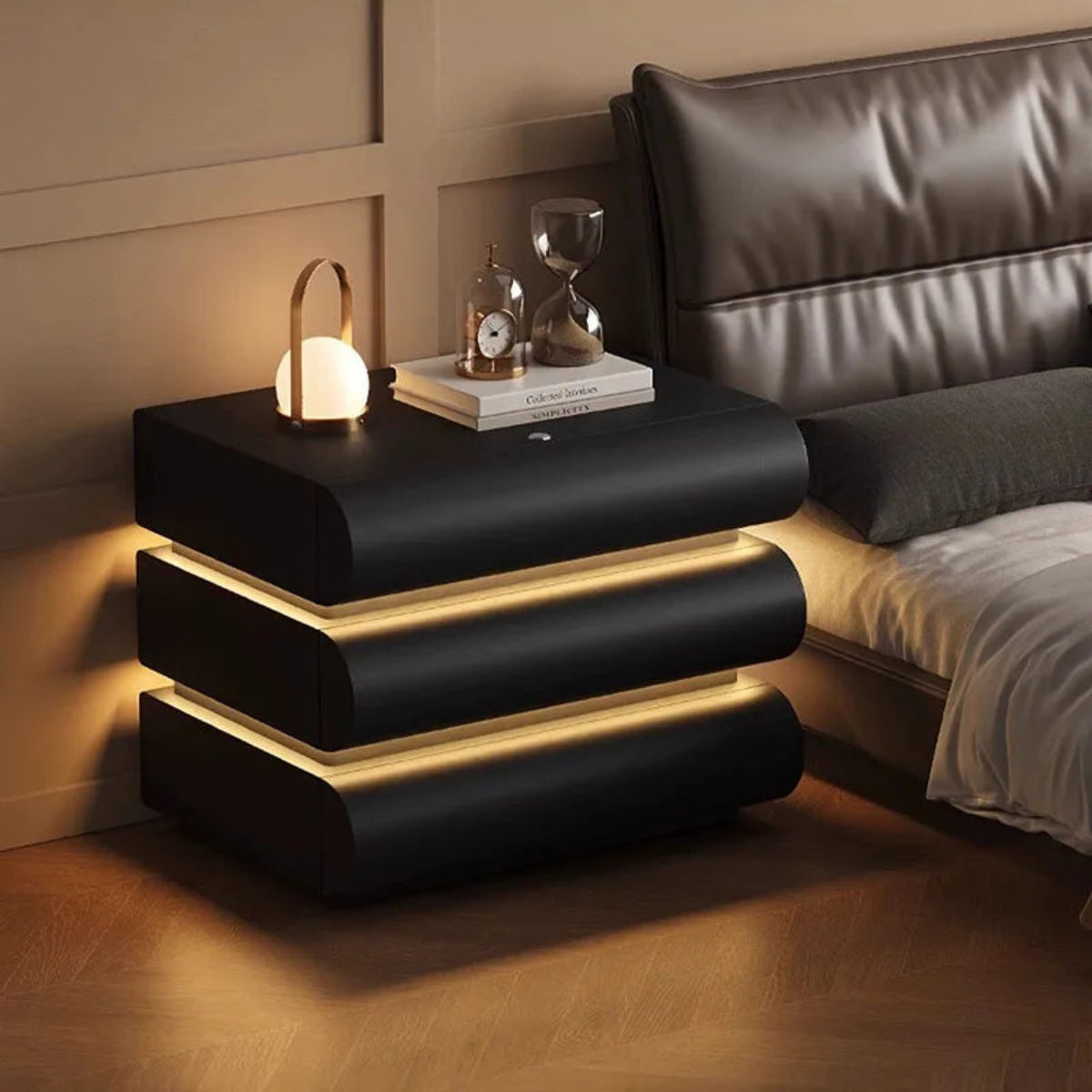 Aura Smart LED luxury nightstand in black with dual warm LED strip glow shown straight-on beside a dark leather bed in a warm luxury bedroom — LivDecor
